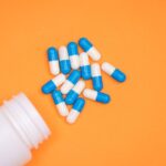 antibiotic medical drug capsule falling from bottle on  orange background