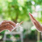 No smoking. Close up of male hands holding cigarettes and proposing it to person. The human arm is gesturing with refusal on bokeh background.