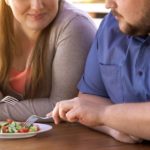 Plump couple eating fresh salad from one plate, weight loss, calories control
