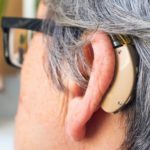 Elderly grey-haired woman with a hearing aid and glasses. Selective focus, close-up.