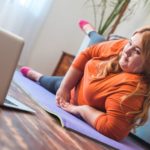 Chubby woman sport at home lying on mat watching workout video on laptop raising leg