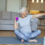 Senior lady smiling at the camera whilst using dumbbells.