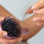 Woman losing hair on hairbrush in hand on bathroom background stock photo