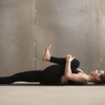 Young woman in Knees to Chest, Apanasana pose, grey studio