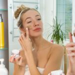 Young beautiful girl applying facial scrub mask on skin.