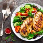 Grilled chicken breast. Fried chicken fillet and fresh vegetable salad of tomatoes, cucumbers and arugula leaves. Chicken meat with salad. Healthy food. Flat lay. Top view. Dark background