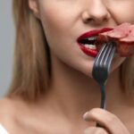 Woman Eating Meat. Closeup Of Beautiful Female Face Biting Meat