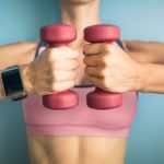 Fit girl holding weights and wearing smartwatch.