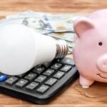 Piggy bank with light bulb, calculator and money on wooden background.