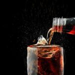 Pour soft drink in glass with ice splash on dark background.