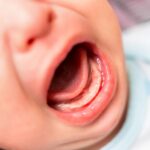 Close up photo of crying 3 months old baby mouth. Bare gums without teeth.