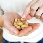 Young woman hands holding and picking up a pistachios nuts at home.