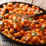 Spicy Middle Eastern chickpea food with eggplant, tomatoes, onions, herbs and spices closeup on a plate. horizontal