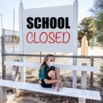 Covid-19 outbreak schools closures. Sad and bored Schoolgirl kid with face mask feeling depressed and lonely outside her closed school. Restrictions and lockdown as Coronavirus containment measures.