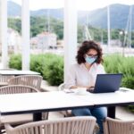 Young woman working safety in empty cafe outdoors. Social distancing in quarantine. Freelancer