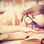tired student girl with glasses sleeping on books in library