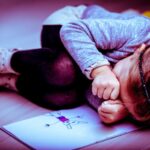 Upset little girl curled up next to her drawing