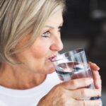 Senior woman drinking water in the kitchen.